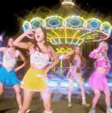 a group of girls are dancing in front of a carousel at night