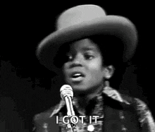 a young man in a cowboy hat is singing into a microphone and saying `` i got it '' .