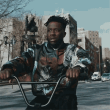 a man wearing a jacket with a wolf on it rides a bike down a city street