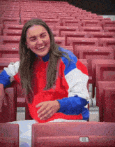 a woman in a red white and blue jacket laughs while sitting in a stadium seat with the number 22 on it