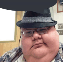 a fat man wearing glasses and a fedora looks at the camera