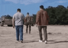 three men are walking down a dirt road in front of a military vehicle .