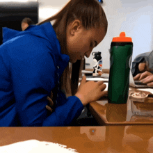 a woman in a blue jacket sits at a table with a gatorade bottle on it