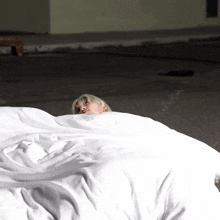 a person is laying on the ground under a white blanket