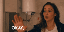 a woman holds up her hand in front of a sign that says " okay "