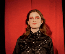 a woman wearing red eye shadow and a black shirt with white embroidery