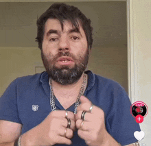 a man with a beard wearing rings and a blue shirt that says r on it