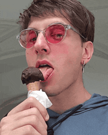 a young man wearing red sunglasses is licking a chocolate ice cream cone