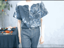 a man wearing a blue shirt and blue jeans is standing in front of a table