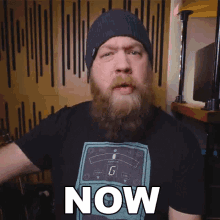 a man with a beard wearing a beanie and a shirt that says now