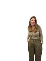 a woman wearing a grey top and khaki pants smiles with her hands in her pockets