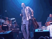 a man singing into a microphone while holding a guitar in front of a mapex drum
