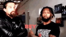 two men are standing next to each other and the word bey is on the wall behind them