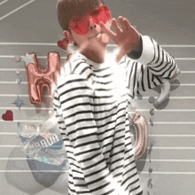 a man wearing a striped shirt and red sunglasses stands in front of balloons that say h