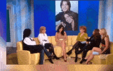 a group of women sit on a couch in front of a picture of a man
