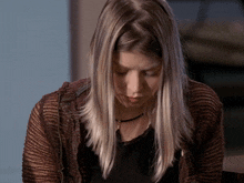 a woman with long blonde hair is wearing a black shirt and a brown cardigan