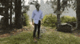 a man in a white shirt and jeans is standing in the middle of a forest .