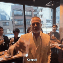 a man in a suit holds a glass and says kanpail