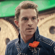 a man in a blue suit with a red flower in his pocket is looking at the camera .