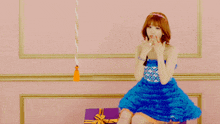 a woman in a blue dress is sitting next to a gift box