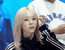 a woman with blonde hair is wearing a blue jacket with white stripes
