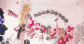 a group of women are dancing in front of a wall of balloons and confetti