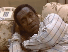 a man in a plaid shirt is laying on a couch next to a phone .