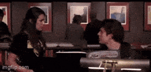 a man and a woman are looking at each other in a room with images on the wall behind them ..