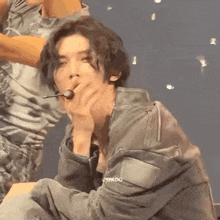 a man in a leather jacket is sitting on a stage with a microphone in his hand .