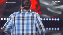 a woman in a plaid shirt is standing on a stage in front of a tv screen that says martes de la voz