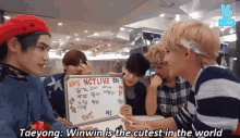 a group of young men are sitting around a table with a white board that says nctlive on it .