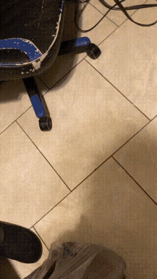 a person 's foot is on a tiled floor next to a blue chair