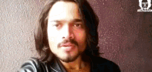 a man with long hair and a beard is wearing a black jacket