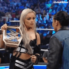 a woman is holding a wrestling championship belt and talking to another woman in a wrestling ring .