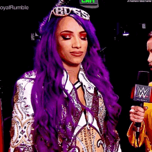 a woman with purple hair is holding a microphone and wearing a crown .