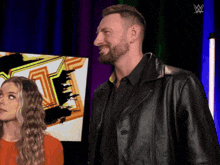 a man in a black leather jacket stands next to a woman in an orange shirt
