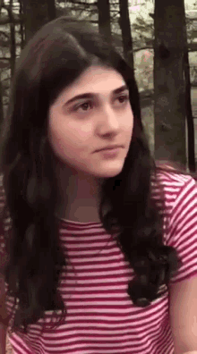 a girl with long hair is wearing a striped shirt and looking at the camera .