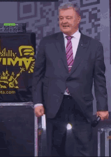 a man in a suit and tie stands in front of a sign that says ally vimtv