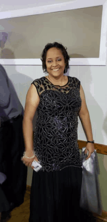 a woman wearing a black dress is smiling and holding a cell phone