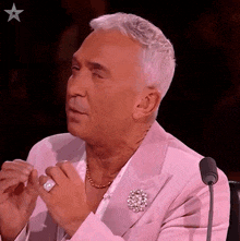 a man in a pink suit is sitting in front of a microphone with his hands folded