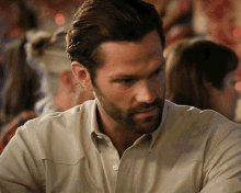 a man with a beard wearing a tan shirt is looking down