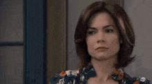 a woman with short brown hair is wearing a floral shirt and making a serious face .
