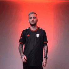 a man wearing a black adidas shirt stands in front of a red wall
