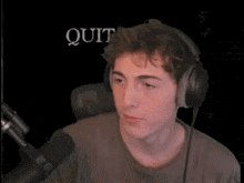 a man wearing headphones is sitting in front of a microphone with the word quit in the background
