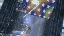 a woman holding a wand in front of a colorful flag with the letter v on it