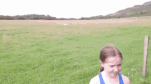 a young girl in a blue tank top stands in a field