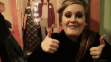a woman giving a thumbs up in front of a picture of a man in a suit