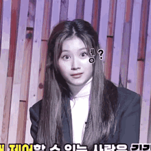 a woman in a suit is standing in front of a wooden wall with a question mark on her face .