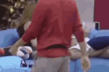 a man in a red shirt is standing next to a blue couch .