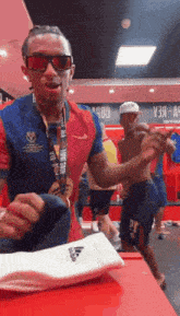 a man wearing sunglasses is standing in a locker room holding a towel .